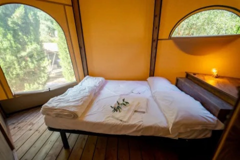 Knus bed in Tipi Lodge bij Trasimeno Glamping Resort, Italië, met houten vloer en grote ramen.