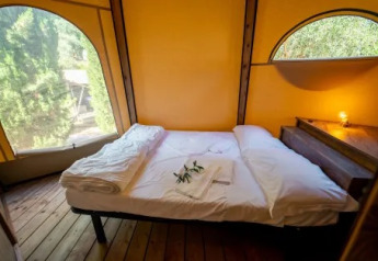 Knus bed in Tipi Lodge bij Trasimeno Glamping Resort, Italië, met houten vloer en grote ramen.
