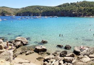 Scenic view of Wecamp L'Escala Punta Mila, Catalonia, Spain, with boats, swimmers, rocks and clear water.