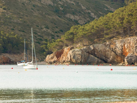 Twee zeilboten liggen voor anker in rustig water omringd door rotsachtige heuvels bij L'Escala, Spanje.
