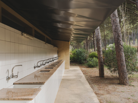 Zona de lavabos exteriores con varios grifos en Wecamp L'Escala Punta Mila, rodeada de pinos.