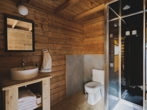Badkamer in Lodge ‘Duplex Plus Montgrí’ met houten wanden, douche, lavabo en toilet bij Wecamp L'Escala Punta Mila.