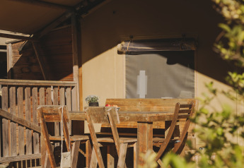 Set da pranzo in legno su veranda davanti a tenda safari, circondato dal sole e dalla natura mediterranea.