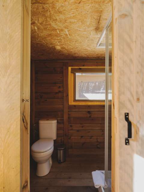 Badkamer met houten wanden, toilet en raam in een safaritent bij Lodge Family Plus Montgó, Wecamp L'Escala Punta Mila.