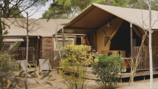 Buitenaanzicht van de Lodge Family Plus Montgó safaritent met houten terras, stoelen en natuurlijke omgeving.