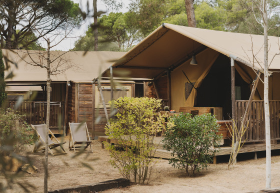 Buitenaanzicht van de Lodge Family Plus Montgó safaritent met houten terras, stoelen en natuurlijke omgeving.