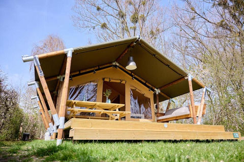 Safari-tent Compact met privé sanitair, houten terras en zitgedeelte in een groene natuurlijke omgeving.