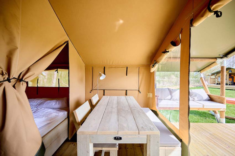 Interieur van een safaritent 'Compact' op Camping Les Bois du Bardelet in Frankrijk met bed en tafel.