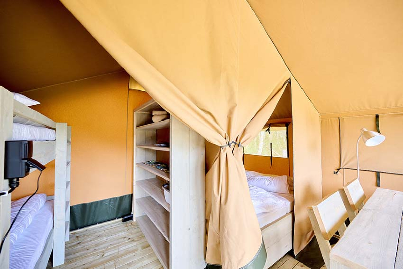 Binnenkant van safaritent 'Compact' op Camping Les Bois du Bardelet met stapelbedden, bed en tafel.