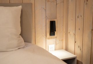 Nærbillede af seng, pude, trævæg og natbord på Ecolodge - Care accessible i Hameau de l'Ourthe, Belgien.