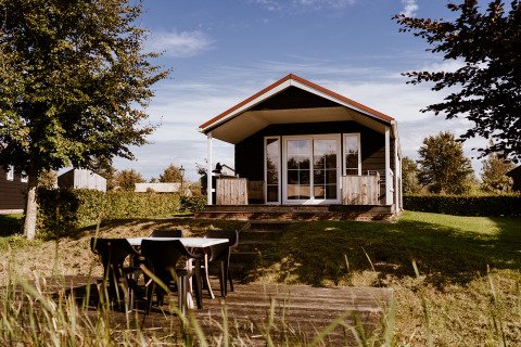 Foto de Group lodge: una cabaña acogedora con porche, mesa exterior y rodeada de naturaleza verde.