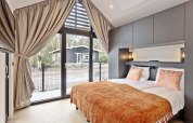 Dormitorio moderno en lodge con grandes ventanas, cortinas, cama doble y vistas al jardín y casa exterior.