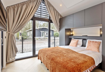 Dormitorio moderno en lodge con grandes ventanas, cortinas, cama doble y vistas al jardín y casa exterior.