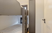Habitación pequeña en una cabaña con litera, armario y dos ventanas pequeñas, decorada de forma sencilla.