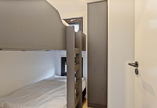 Petite chambre de lodge avec lits superposés, armoire et deux petites fenêtres, décoration épurée et claire.