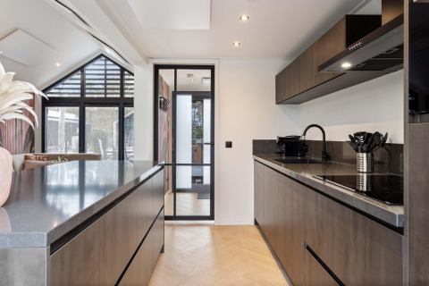 Cocina moderna en lodge con muebles oscuros, puerta de cristal y suelo de madera clara y elegante.