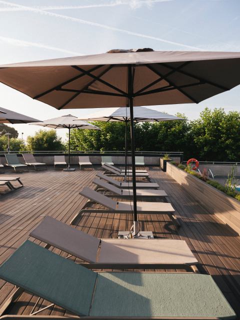 Lettini prendisole su terrazza in legno con ombrelloni al Wecamp San Sebastián nei Paesi Baschi, Spagna.