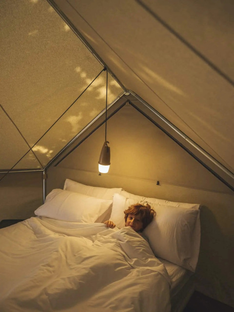 Personne allongée dans un lit douillet avec une lumière douce à l'intérieur d'une tente safari confortable.