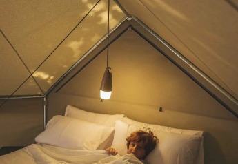 Person entspannt auf einem gemütlichen Bett unter sanftem Licht im Inneren eines Safari-Zeltes.