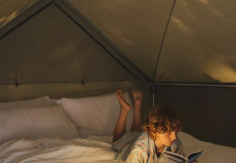 Ein Kind liest ein Buch auf einem Bett im Inneren eines Safarizeltes mit warmem, gemütlichem Licht.