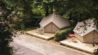 Zwei Bell Tent Plus Safari-Zelte mit Holzterrassen und Sitzbereichen in einem bewaldeten Campingplatz.
