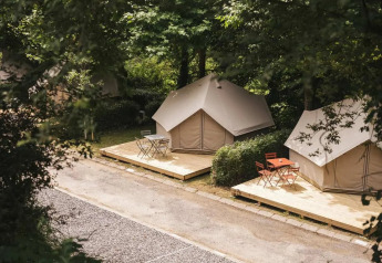 Zwei Bell Tent Plus Safari-Zelte mit Holzterrassen und Sitzbereichen in einem bewaldeten Campingplatz.