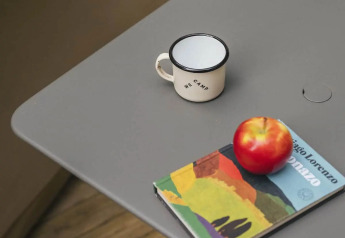 Table grise sous tente safari avec une tasse émaillée, une pomme rouge et un livre coloré dessus.