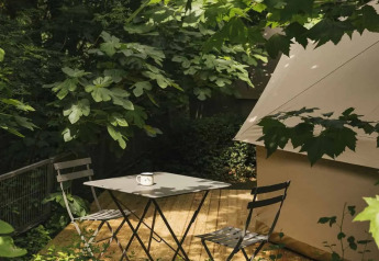 Área de descanso al aire libre junto a una tienda safari, rodeada de vegetación y árboles frondosos.