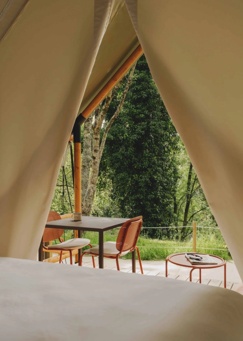 Uitzicht vanuit een safari-glamping tent met open ingang, tafel en stoelen, omringd door bomen in Spanje.