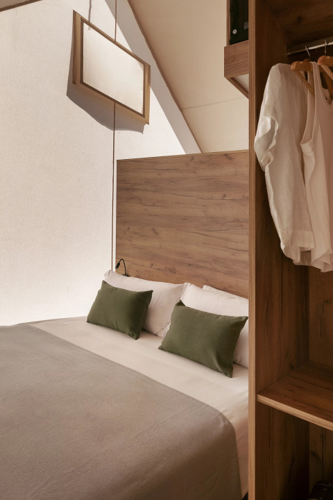 Interior de una tienda glamping en Wecamp San Sebastián con cama doble, cojines verdes y armario abierto.