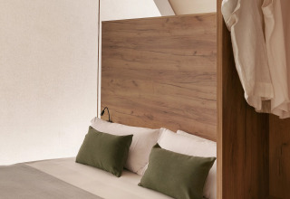 Interior de una tienda glamping en Wecamp San Sebastián con cama doble, cojines verdes y armario abierto.
