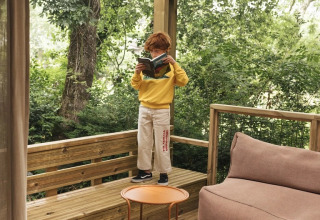 Kind leest een boek op het houten terras van Mobil Home Family Plus bij Wecamp San Sebastián, te midden van groen.
