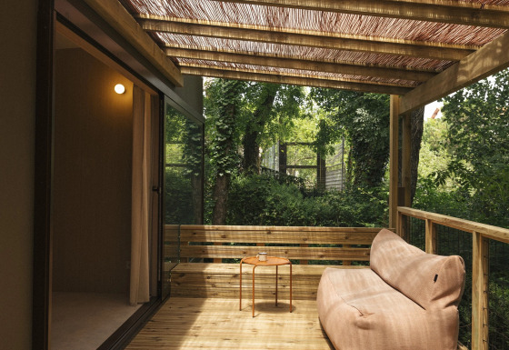 Houten terras bij Mobil Home Family Plus met comfortabele bank, klein tafeltje en gevlochten dakbedekking.