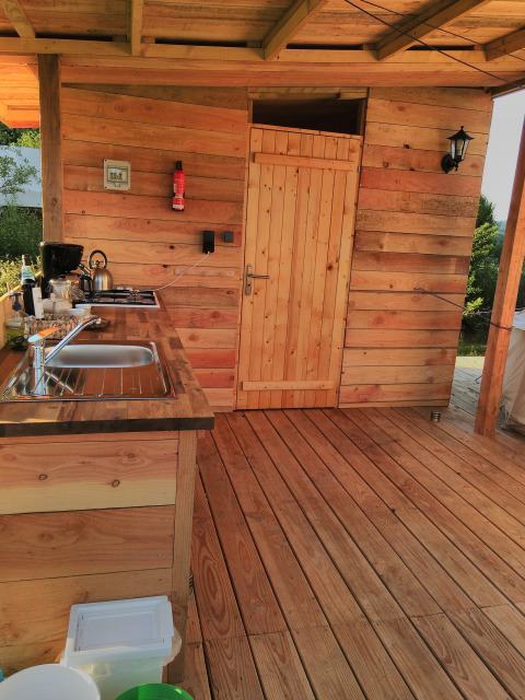 Cucina all'aperto in legno presso Sybley Apex tent, Camping Junora, Francia, con lavello e porta.
