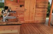 Wooden outdoor kitchen at Sybley Apex tent, Campsite Junora in France, featuring sink and door.