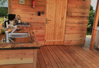 Cucina all'aperto in legno presso Sybley Apex tent, Camping Junora, Francia, con lavello e porta.