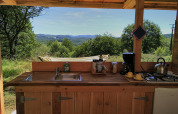 Outdoor kitchen at Bell XL family tent at Campsite Junora, France, overlooking hills and lush greenery.