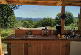 Outdoor kitchen at Bell XL family tent at Campsite Junora, France, overlooking hills and lush greenery.