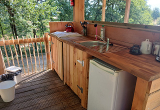 Angolo cottura in legno all’aperto con lavello, mini frigo e vista bosco nella tenda Bell al Camping Junora.
