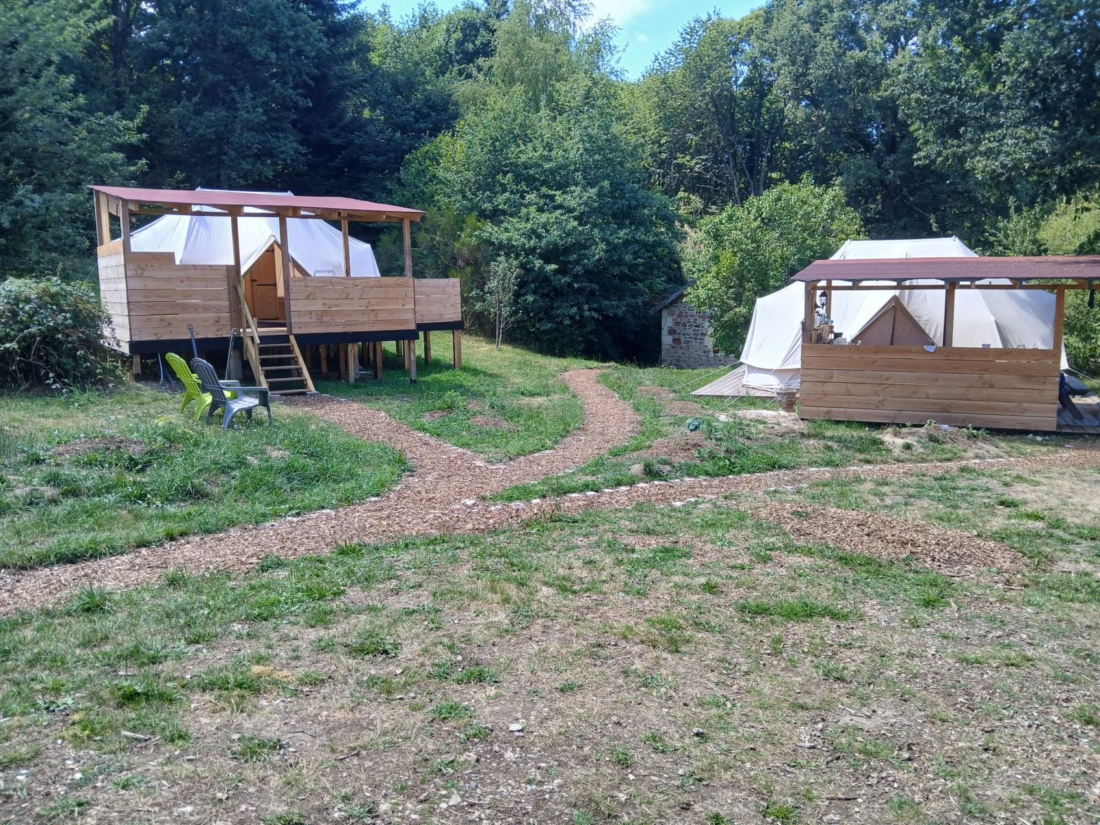 Twee grote tenten op houten terrassen bij Emperor Bell Tent, Campsite Junora in Frankrijk, omringd door bos.