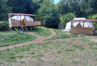 Due grandi tende con terrazze in legno all'Emperor Bell Tent, Campeggio Junora, Francia, tra gli alberi.