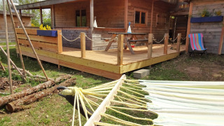 Tree house named Eco-Chalet EXTRA with wooden deck, hammock, and colorful towel outside.