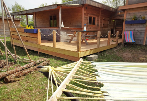 Boomhut genaamd Eco-Chalet EXTRA met houten terras, hangmat en kleurrijke handdoek buiten.