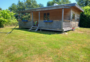 Eco-chalet di lusso autosufficiente con facciata in legno e veranda, immerso nel verde.