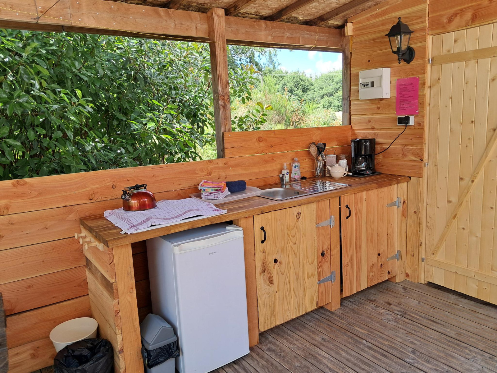 Buitenkeuken van hout met gootsteen, koffiezetapparaat en minikoelkast, uitzicht op de natuur.