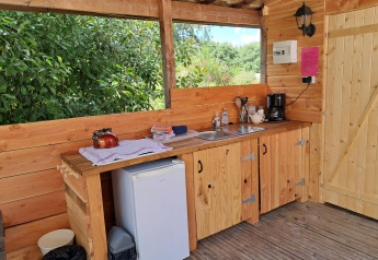 Cucina in legno all'aperto con lavello, macchina da caffè, mini frigo e vista sulla natura.