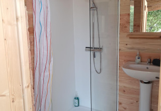 Bagno con doccia e lavandino in una cabina di legno nella tenda Sibley Apex al Campsite Junora in Francia.
