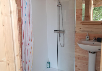 Bagno con doccia e lavandino in una cabina di legno nella tenda Sibley Apex al Campsite Junora in Francia.