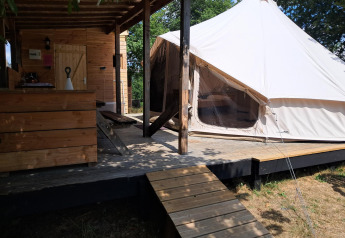 Vista esterna di una tenda Sibley Apex e una cabina in legno su un ponte, ideale per il glamping.