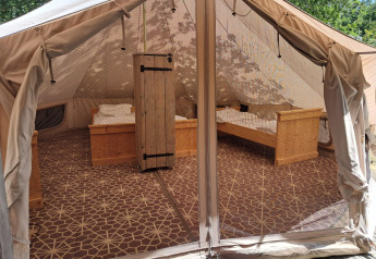 Vista interna di una tenda Sibley Apex con quattro letti in legno e tappeto al Campeggio Junora in Francia.